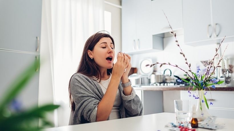 Woman sneezing from allergies about to take medicine from allergist